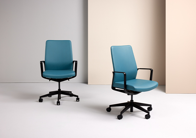 Two modern teal office chairs with black bases, positioned on a light floor against a neutral backdrop.